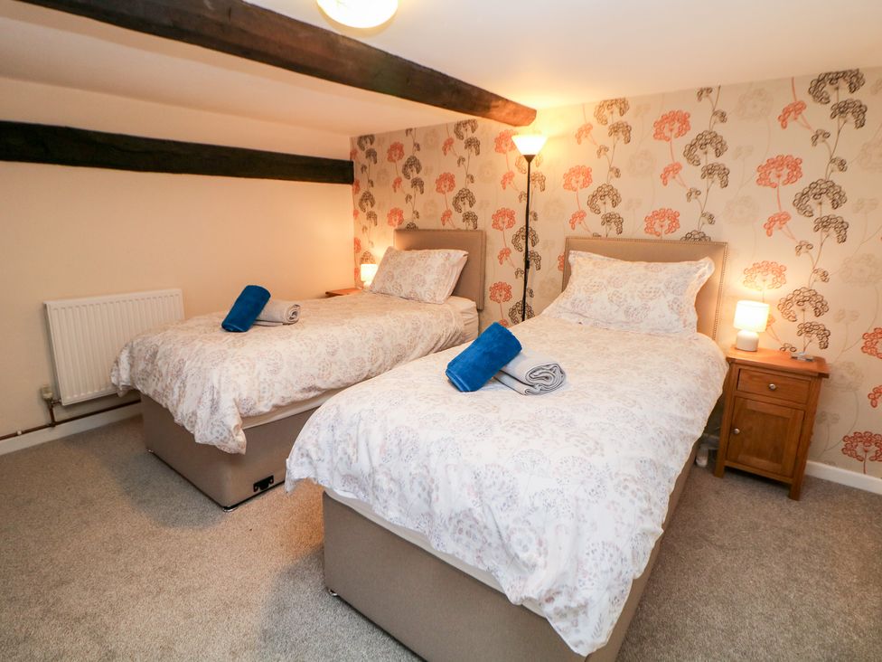 A bedroom with two single beds bedside tables lamps and a floor lamp at Wilson Eyre Cottage in Castleton Peak District
