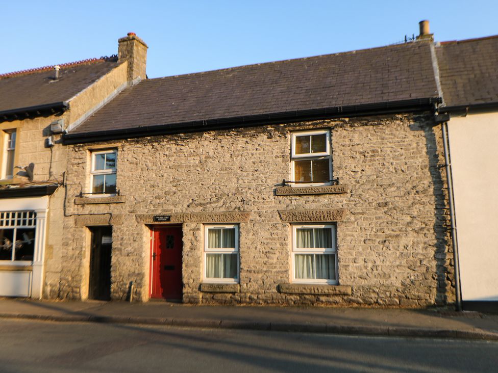 A stone cottage with a red door and four windows on a street at Wilson Eyre Cottage in Castleton Peak District