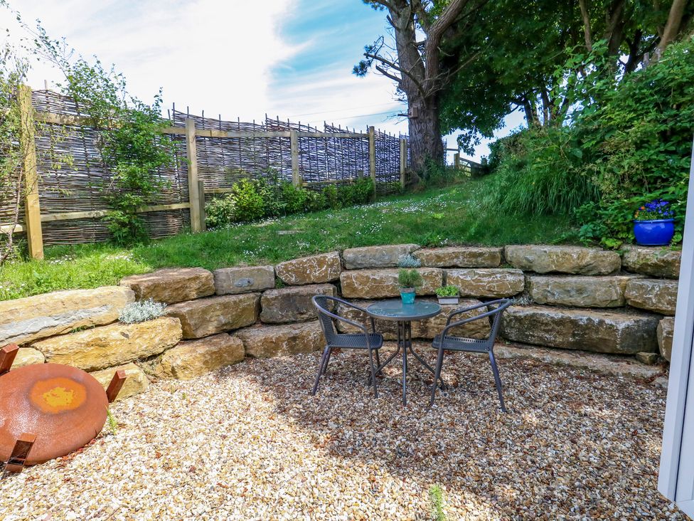 An outdoor patio area with two chairs and a small round table on gravel surrounded by stone retaining walls and greenery at The Cabin in Swanage