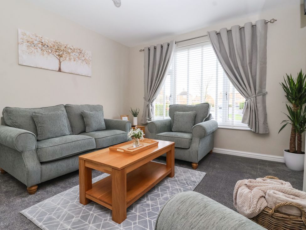 A living room with grey sofas wooden coffee table and window with grey curtains at The Coastal Hideaway in Hornsea