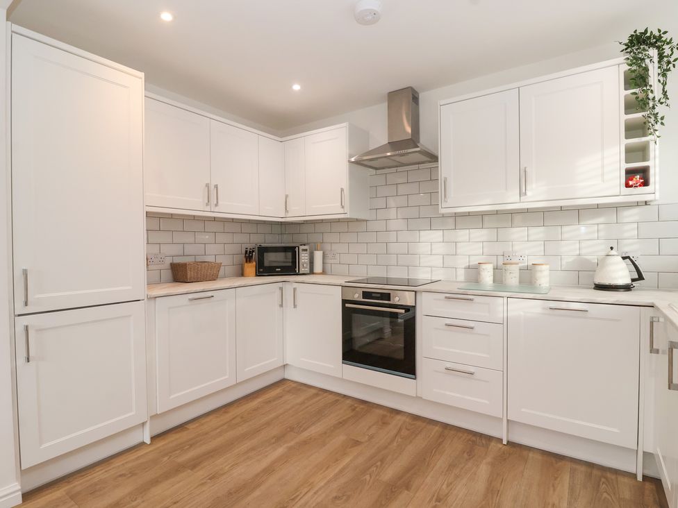 A kitchen with white cabinets oven microwave kettle and wooden floor at The Coastal Hideaway in Hornsea