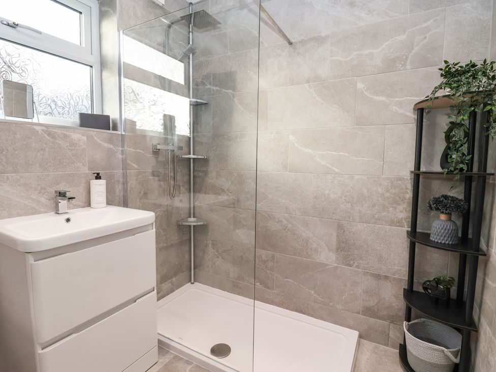 A bathroom with a shower area sink and shelving unit with plants at The Coastal Hideaway in Hornsea