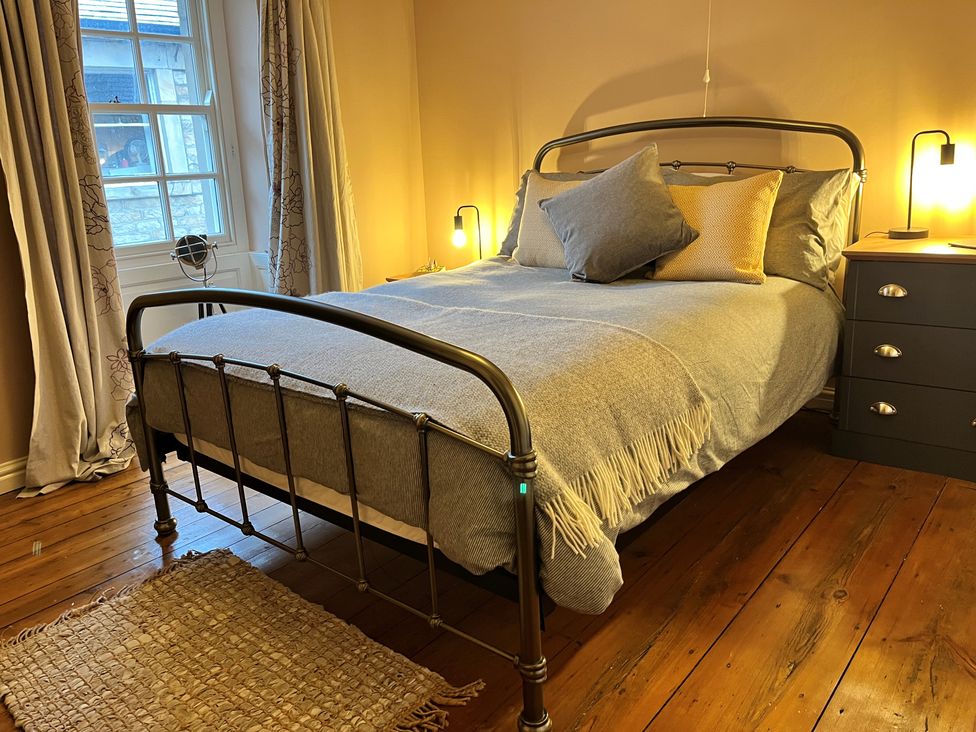 A bedroom with a metal frame bed with pillows and a blanket with wooden floor and a window with curtains at 5 Castle Hill in Lancaster