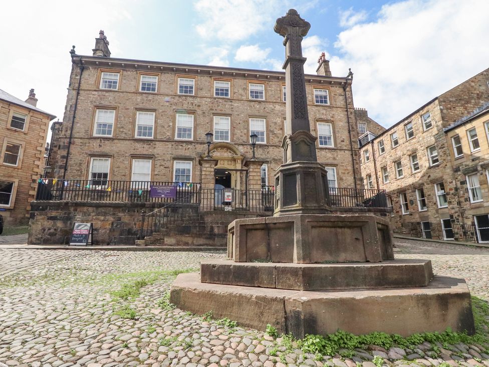 A stone cross monument on a cobblestone street in front of a multi window stone building at 5 Castle Hill in Lancaster