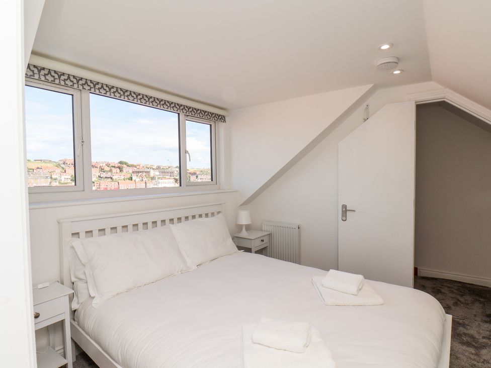 A bedroom with a white bed and bedside tables next to a window showing buildings at Whitby View in Whitby