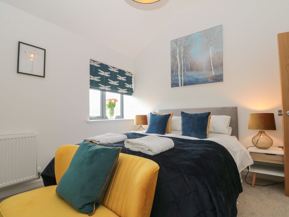 A bedroom with a bed with blue and yellow pillows a yellow chair a window with a dragonfly patterned blind and a painting of trees at Bailey house in Pocklington