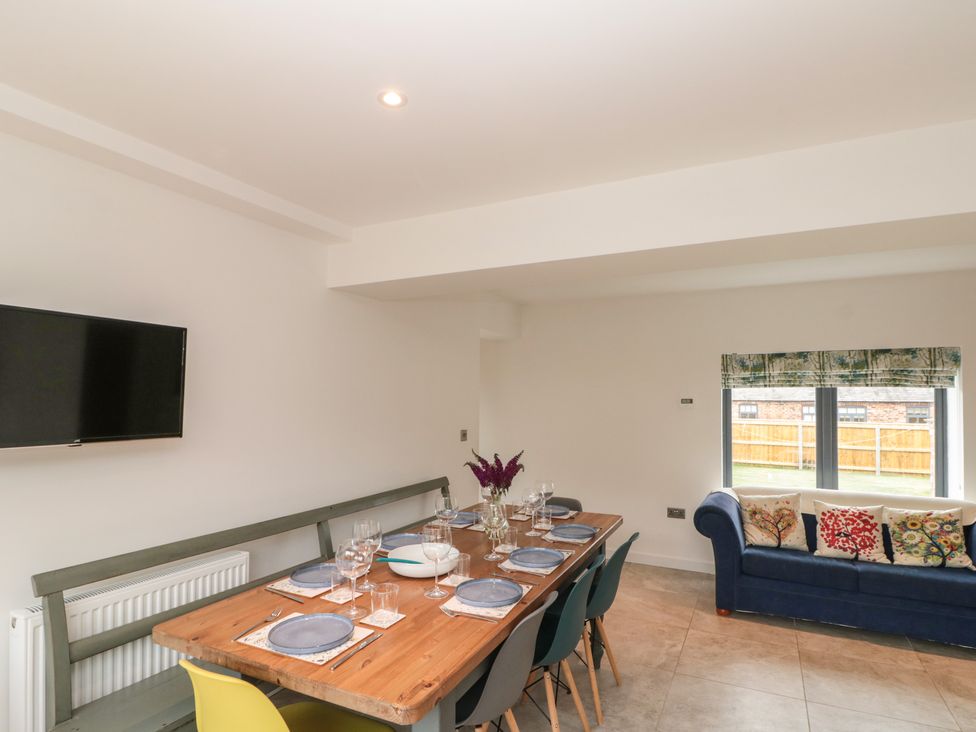 A dining area with a wooden table set for eight and a blue sofa with decorative cushions by a window at Bailey house in Pocklington
