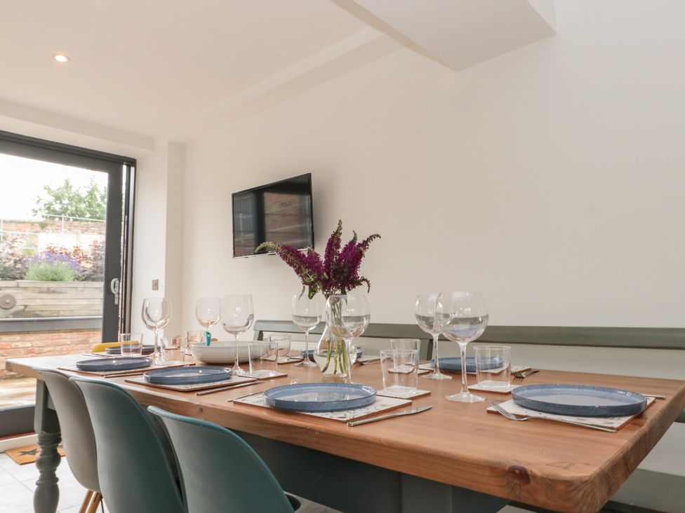 A dining table set with plates glasses and a vase of flowers in a room with a mounted television at Bailey house in Pocklington