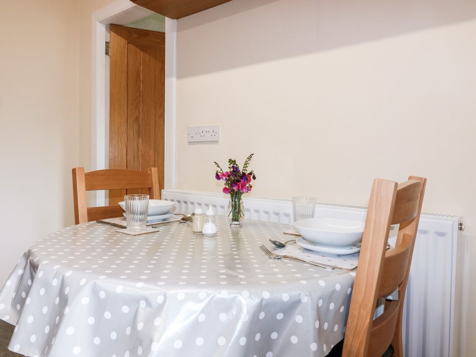 A dining area with a round table covered by a polka dot tablecloth set with two place settings and a small vase of flowers at Katmoget Cottage in Scotstarvit near Ceres