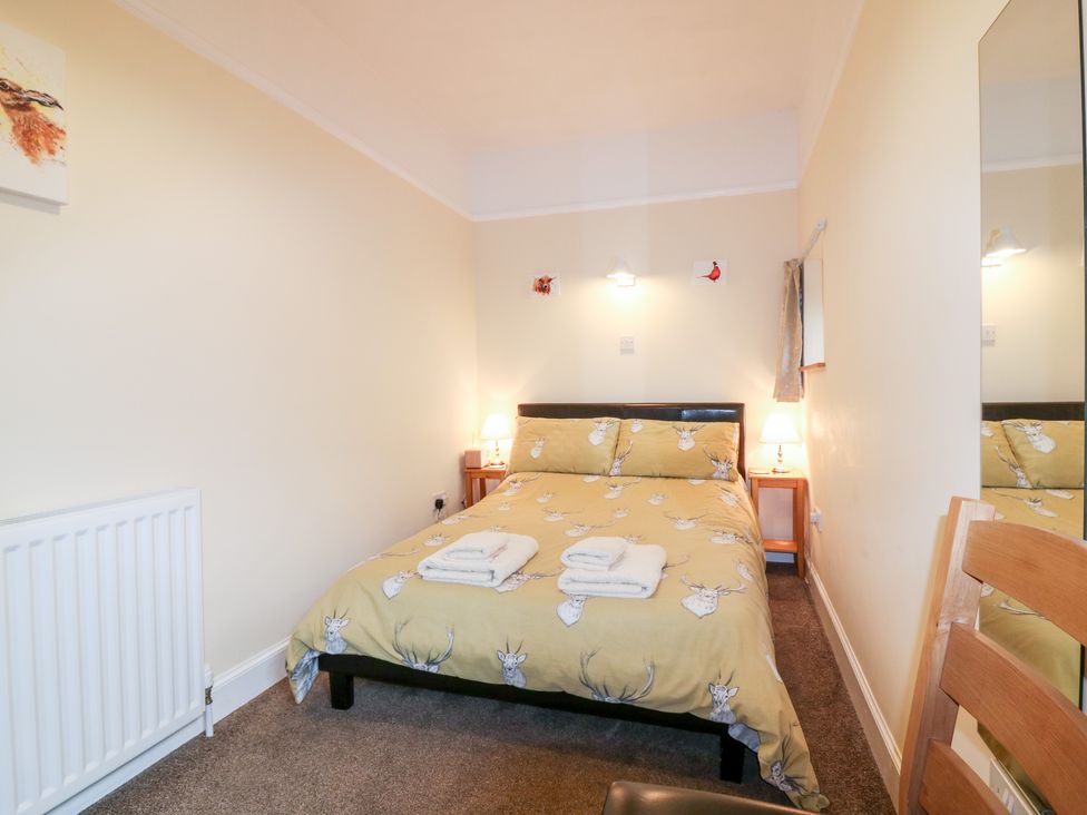 A bedroom with a double bed with animal print bedding two bedside tables with lamps a wooden chair and a radiator at Katmoget Cottage in Scotstarvit near Ceres