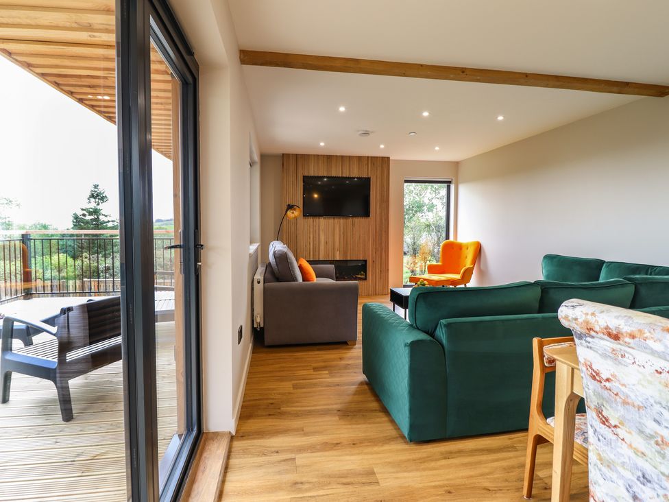 A living room with green and gray sofas and an orange chair next to a patio at Mynydd Y Glyn Lodge in Llanfyllin near Llanrhaeadr-Ym-Mochnant