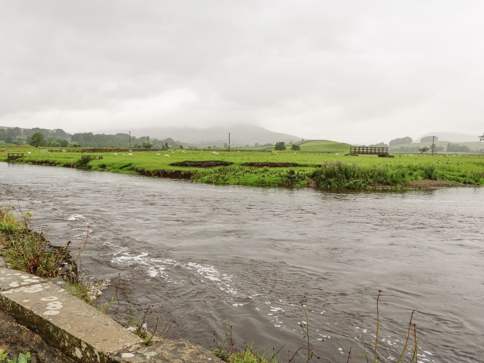A river flowing beside green fields with sheep and hills in the background at Miss Burrow's House in Hawes
