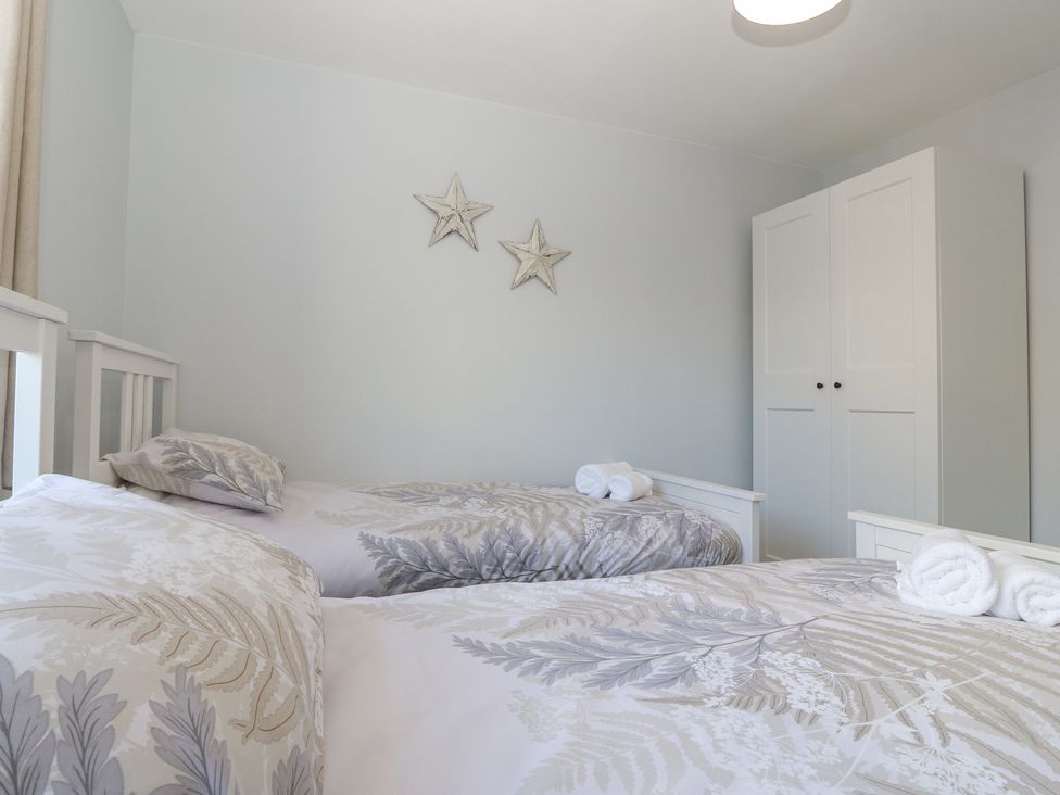 A bedroom with two beds and a white wardrobe with star decorations on the wall at Llwyn Eithin in Benllech