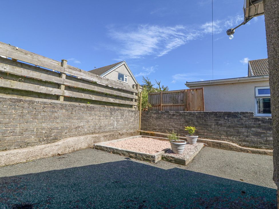 An outdoor patio area with a raised gravel bed and two plant pots surrounded by brick and wooden fences at Llwyn Eithin in Benllech