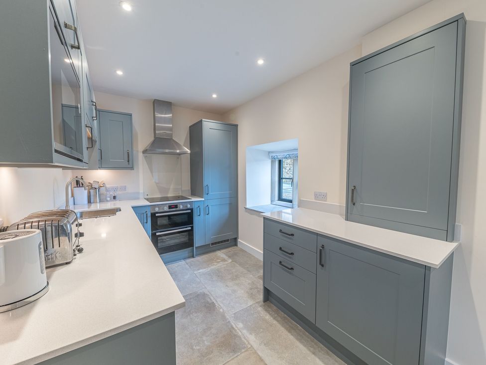 A kitchen with grey cabinets, white countertops, a built-in oven, a toaster, and a small window at No 2 The Coach House in Thornton In Lonsdale