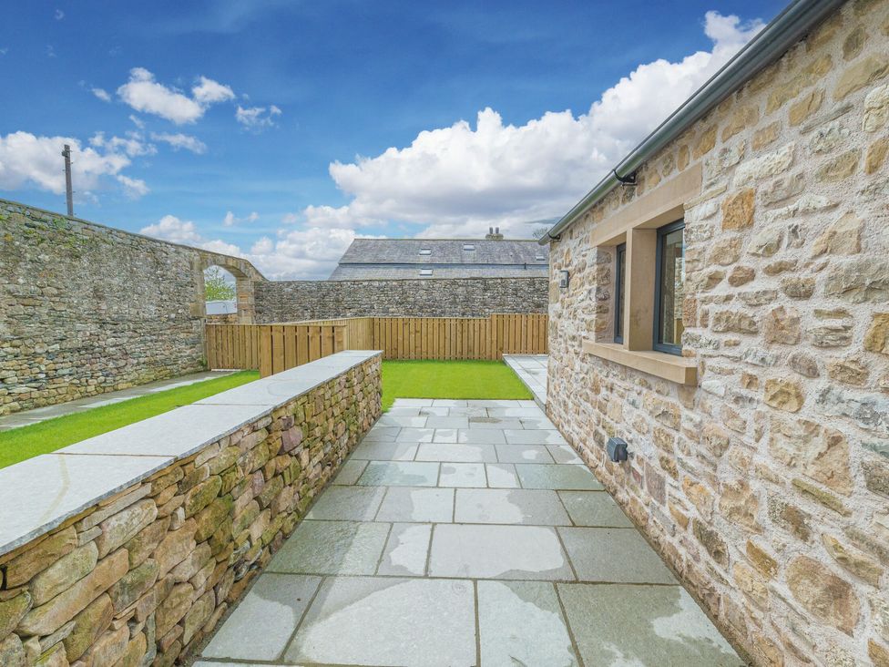 An outdoor patio area with stone walls grass lawn and a paved walkway at No 2 The Coach House in Thornton In Lonsdale
