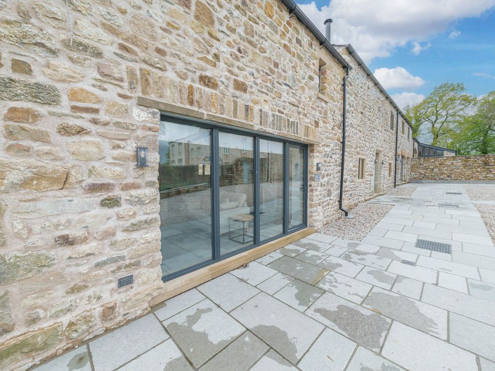 Stone exterior wall with large glass doors and paved walkway at No 2 The Coach House in Thornton In Lonsdale