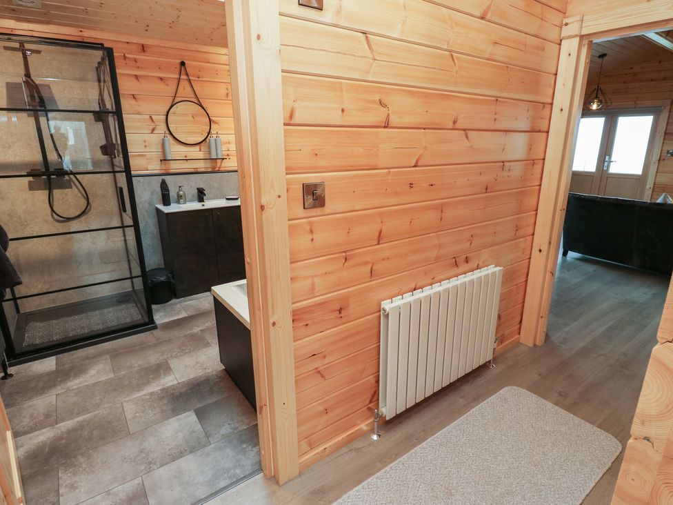 A hallway with wooden walls leading to a bathroom with a glass shower and a living room at Height End Farm Log Cabin Rossendale near Bacup