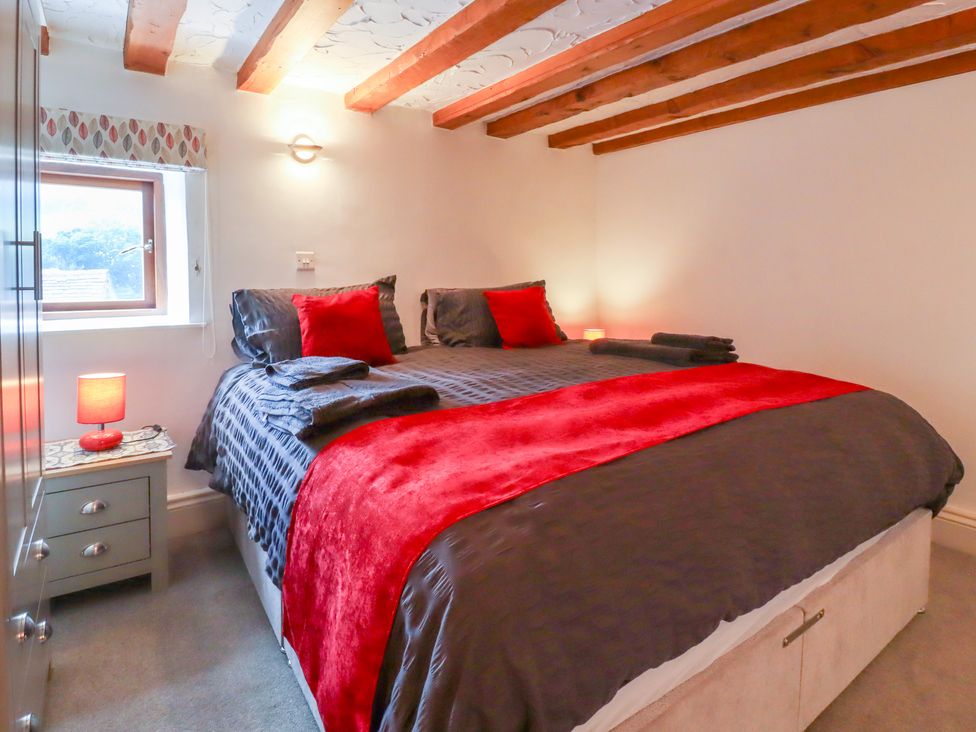 A bedroom with a double bed with grey and red bedding wooden ceiling beams and two bedside tables with lamps at Battery Barn in Kettlewell