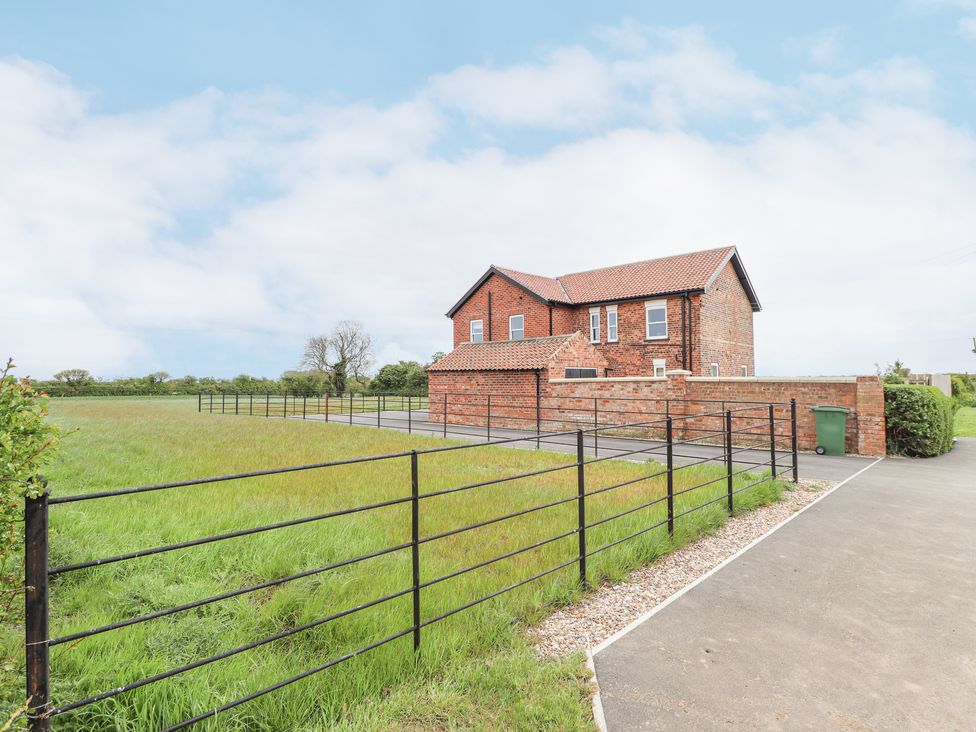 A brick house with a tiled roof next to a grassy field and a metal fence at Foremans Cottage in Withernsea