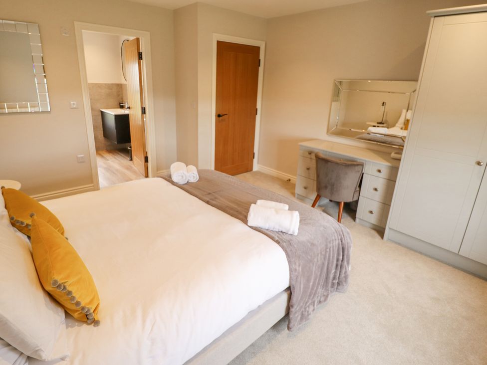 A bedroom with a bed, desk with a chair, wardrobe, and an open door to a bathroom at Foremans Cottage in Withernsea