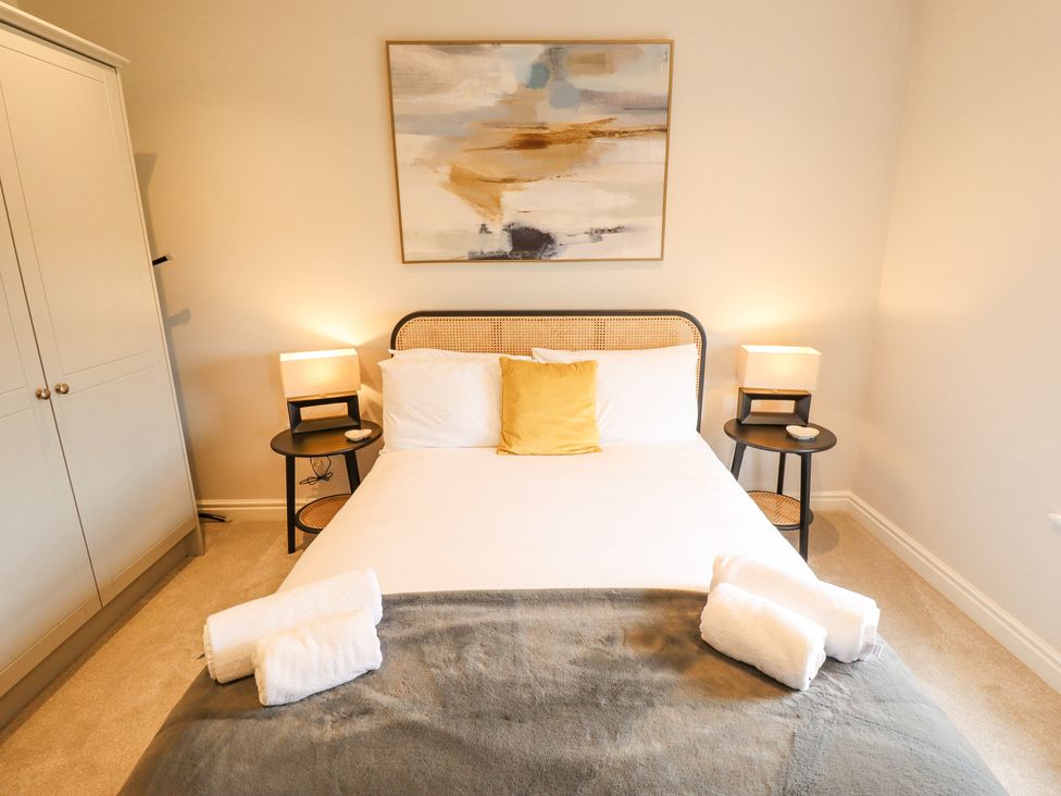 A bedroom with a bed with pillows and towels bedside tables with lamps a wardrobe and a painting on the wall at Foremans Cottage in Withernsea