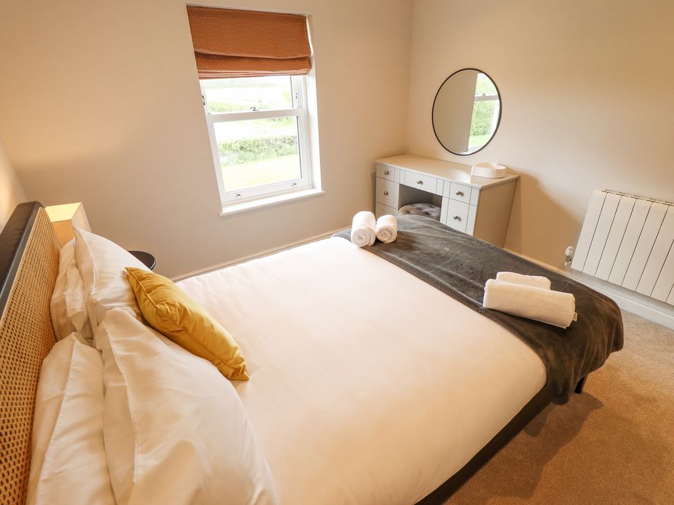 A bedroom with a double bed, a window with a shade, a dresser with a round mirror, and rolled towels on the bed at Foremans Cottage in Withernsea