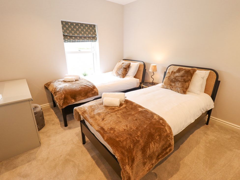A bedroom with two single beds with brown throws and pillows a small bedside table with a lamp and a window with patterned blind at Foremans Cottage in Withernsea
