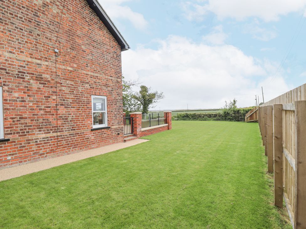 A grassy backyard with a wooden fence and a brick house at Foremans Cottage in Withernsea