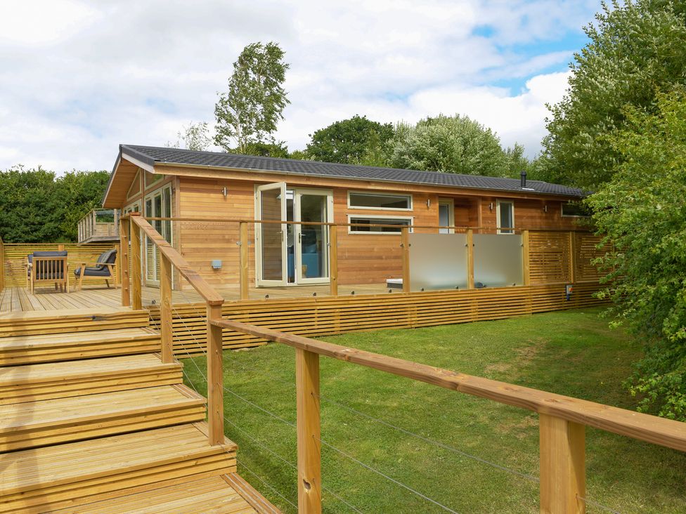 A wooden house with a deck and stairs surrounded by grass and trees at 4 Valley View in Lanreath