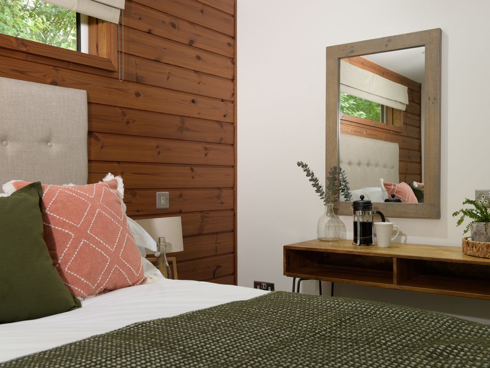 A bedroom with a bed with pillows and a green blanket next to a wooden desk with a mirror and decorative items at 4 Valley View Lanreath