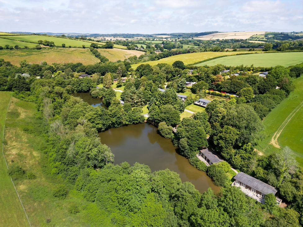 An aerial view of a rural area with two ponds surrounded by trees and scattered houses at 4 Valley View in Lanreath