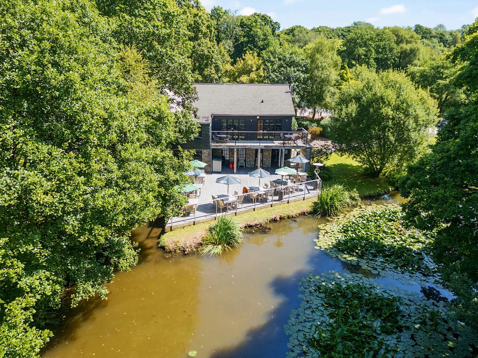 A two-story building with outdoor seating and umbrellas beside a pond surrounded by trees at 4 Valley View Lanreath