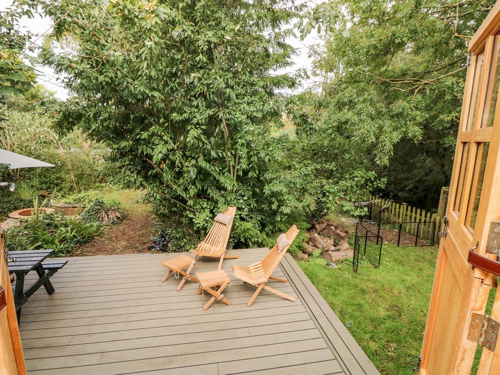 A wooden deck with two wooden chairs and footrests surrounded by trees and garden at The Happy Hut in Sopley near Christchurch