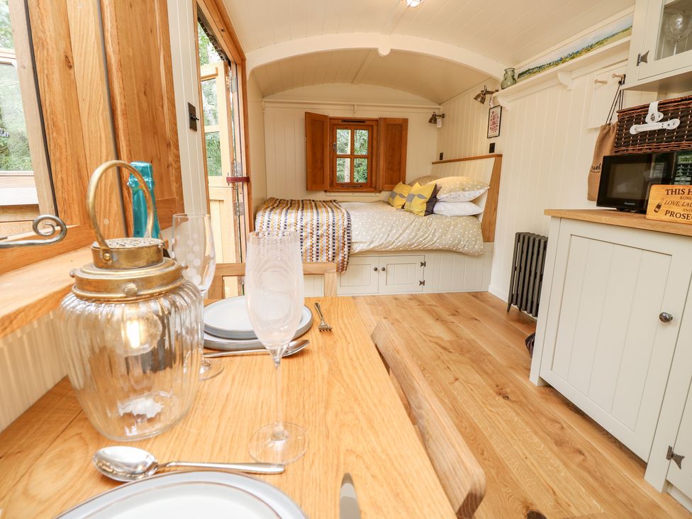 A small dining area with plates glasses and a lantern next to a bed with pillows blankets and wooden window at The Happy Hut in Sopley near Christchurch