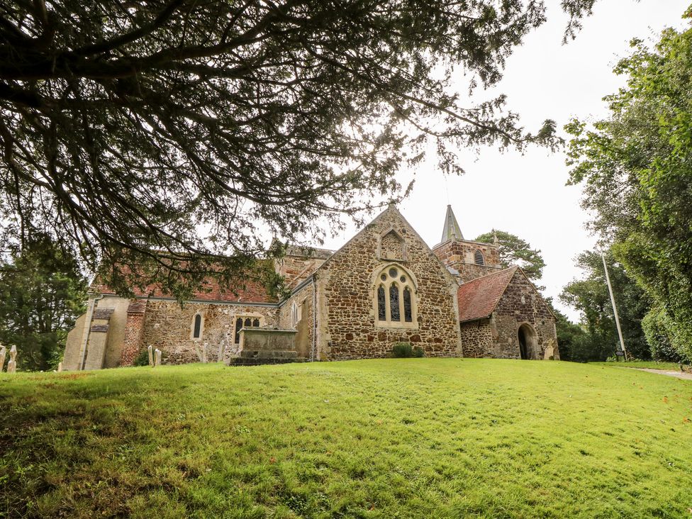 A stone church with a red tiled roof on a grassy slope with trees around at The Happy Hut in Sopley near Christchurch