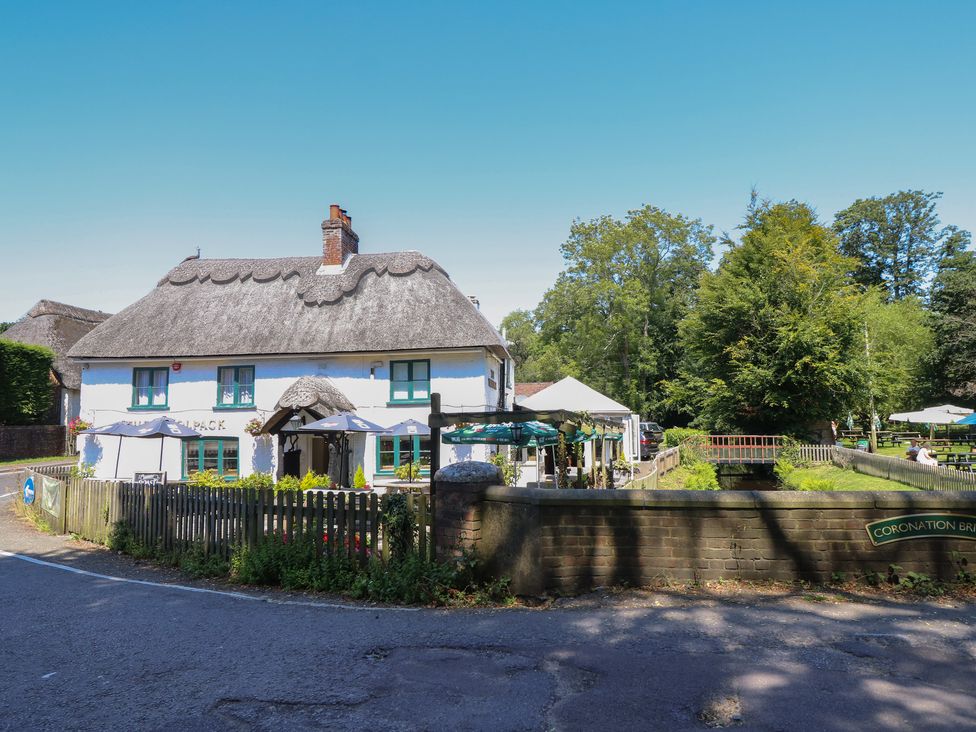 A thatched roof pub with outdoor umbrellas and tables near a small bridge and trees at The Happy Hut in Sopley near Christchurch