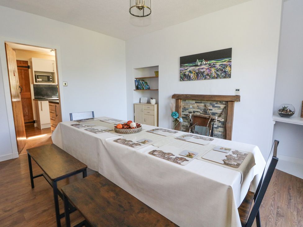 A dining room with a table covered with a white tablecloth and placemats benches and chairs around the table a fireplace and a bookshelf in the background at Callart View in Glencoe