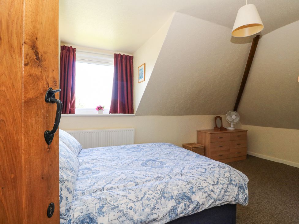 A bedroom with a bed a window with curtains and a dresser with a fan and mirror at Callart View in Glencoe