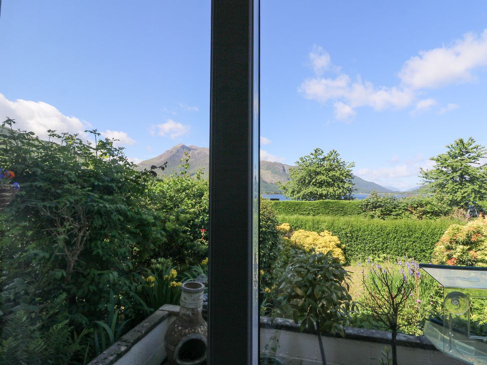 A garden with bushes flowers and trees overlooking mountains behind a glass window at Callart View in Glencoe