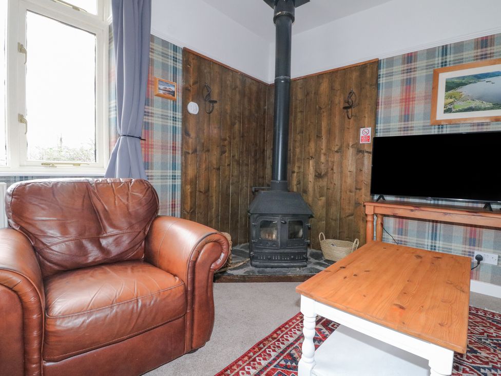 A living room with a brown leather armchair a wood stove a television on a wooden table and a coffee table at Callart View in Glencoe