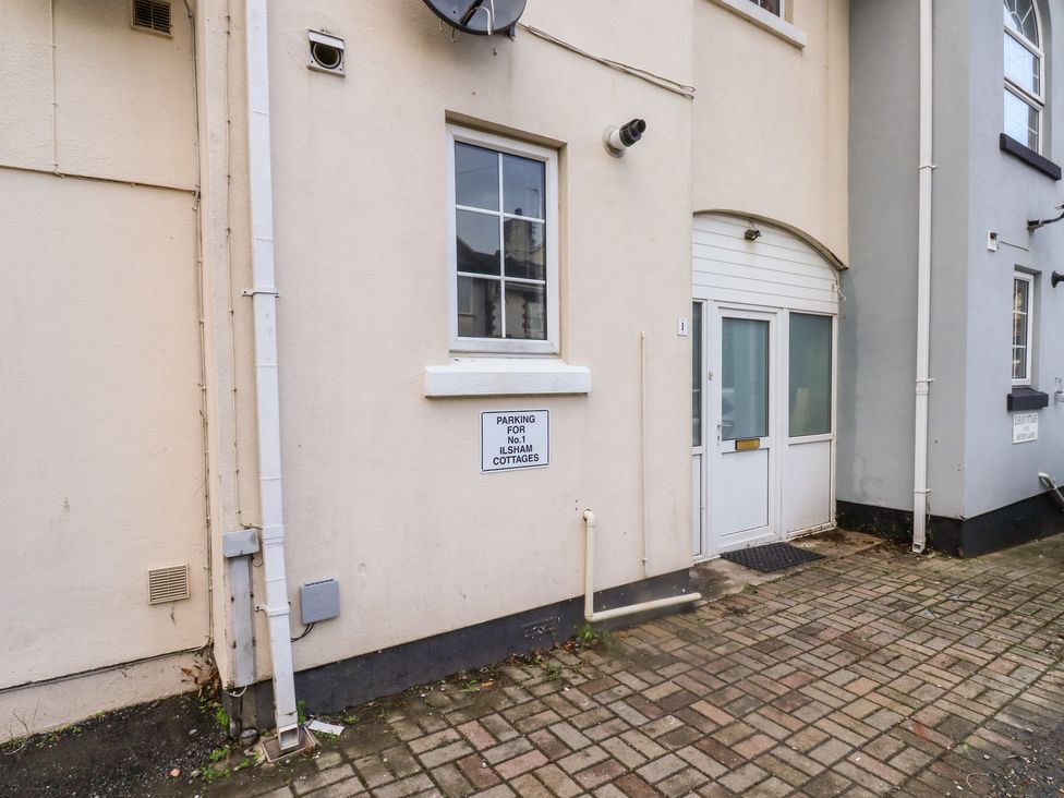An exterior view of a building with a white door and window a sign indicating parking for No 1 Ilsham Cottages on the wall at 1 Ilsham Cottages Torquay