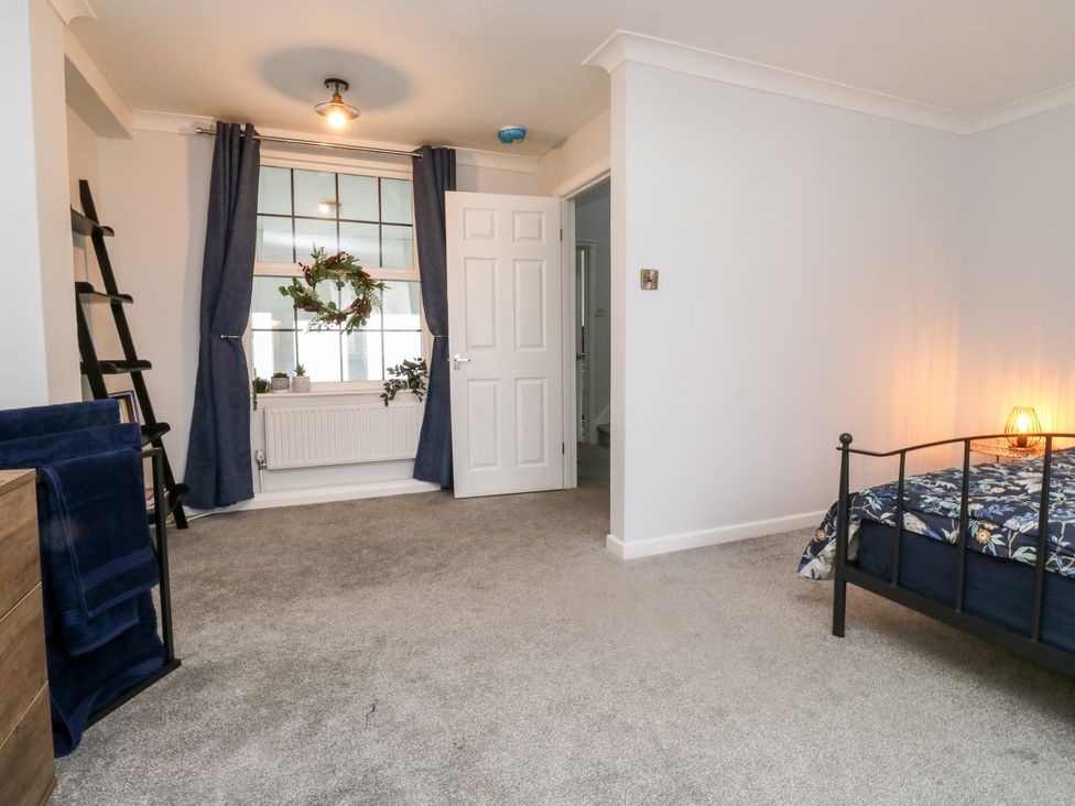 A bedroom with a metal bed frame and floral bedding a window with dark curtains and plants and an open white door at 1 Ilsham Cottages in Torquay