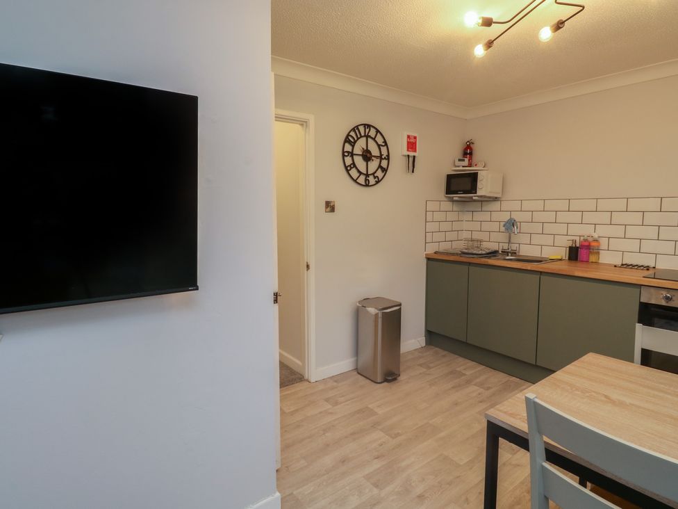 A kitchen area with green cabinets wooden countertops a microwave mounted on the wall a wall clock and a wall-mounted television at 1 Ilsham Cottages in Torquay