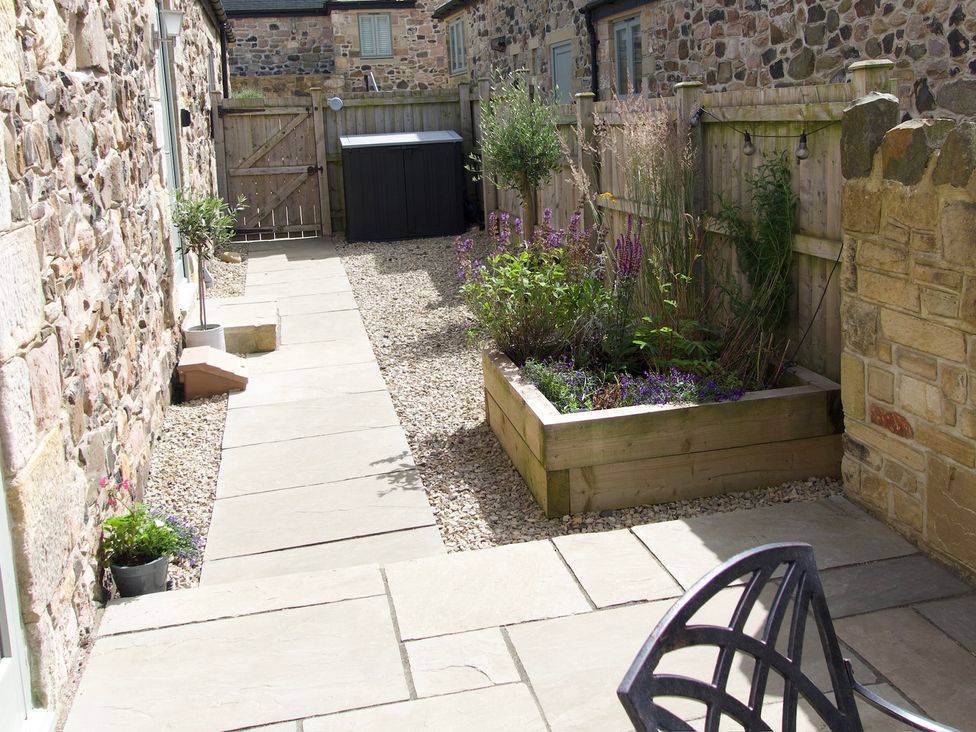 An outdoor patio area with stone paving a wooden raised flower bed and a wooden fence at The Coach House in Bamburgh