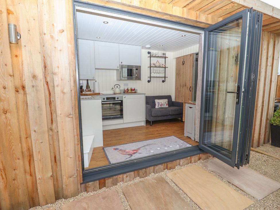 A small kitchen living area with white cabinets gray sofa and glass folding door at Hillside Hut in Radbourne near Ashbourne