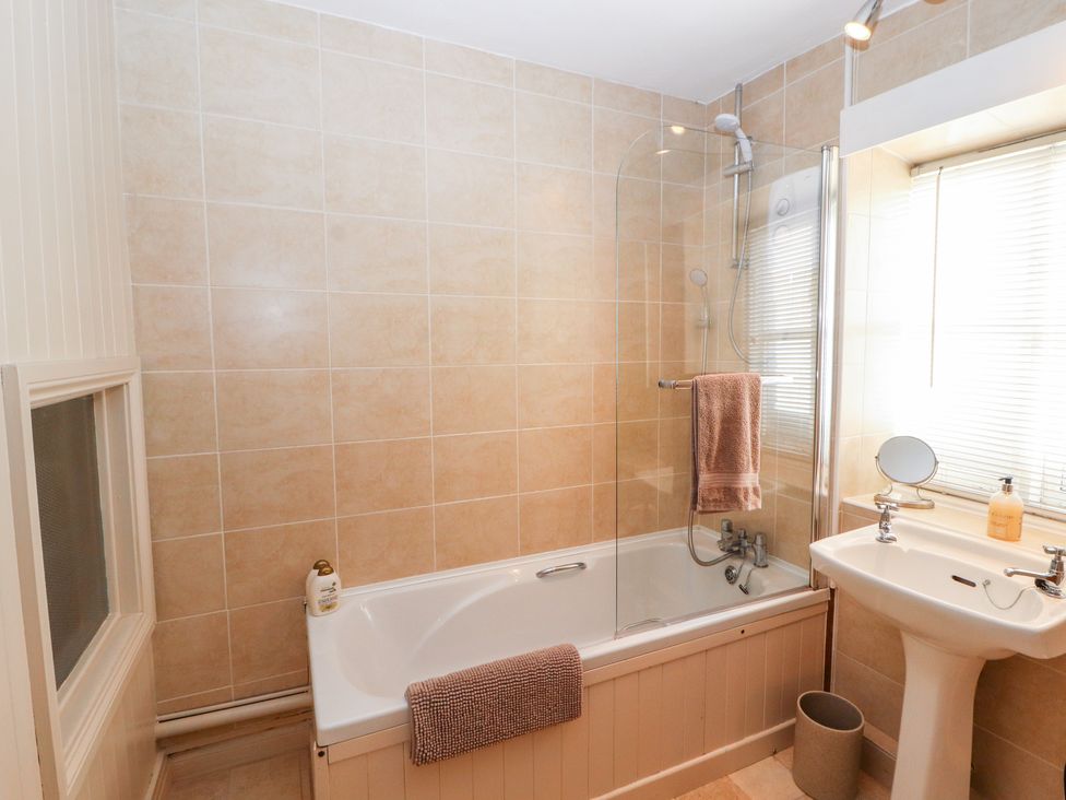 A bathroom with a bathtub shower combination a sink with a mirror and soap dispenser at Market Square Maisonette in Kirkby Lonsdale