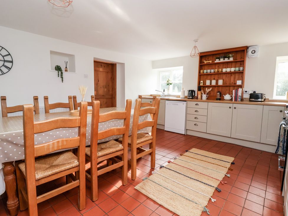 A kitchen with a dining table and chairs wooden shelves with cups and kitchen appliances at Cliff Cottage in Thirsk