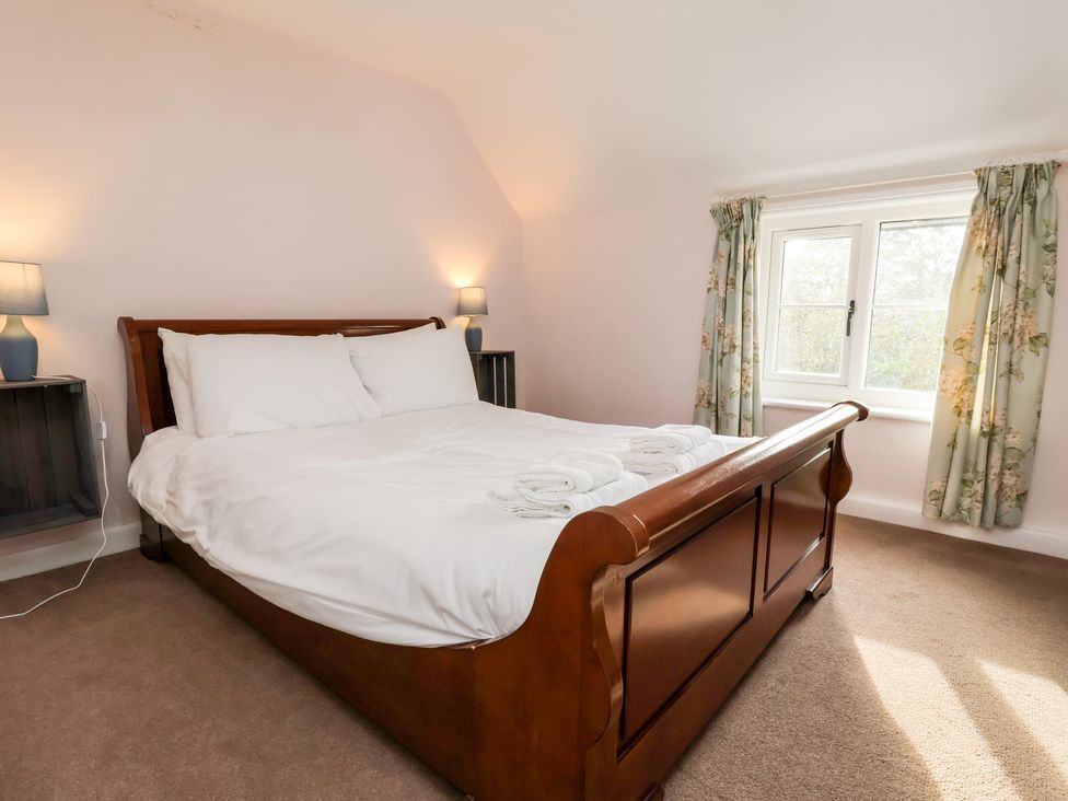 A bedroom with a wooden bed and white bedding by a window with floral curtains at Cliff Cottage in Thirsk