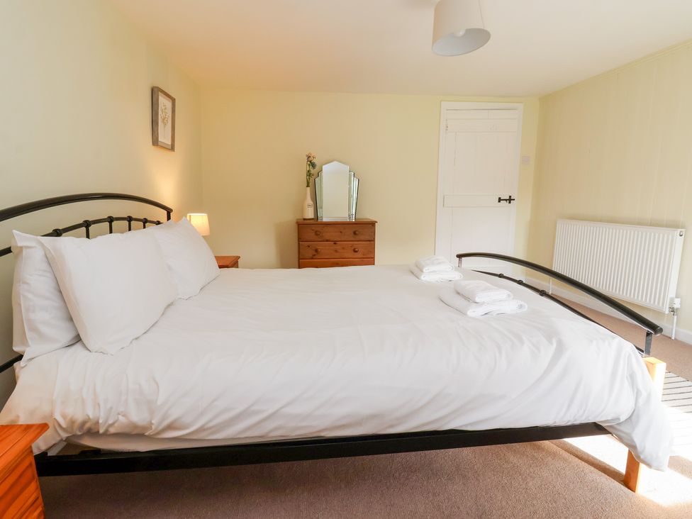 A bedroom with a bed with white linens bedside tables a wooden dresser with a mirror and a door at Cliff Cottage in Thirsk